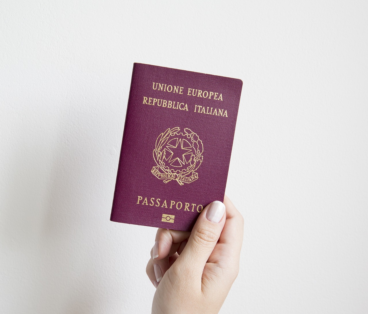 Dłoń trzymająca czerwony włoski paszport na tle ściany