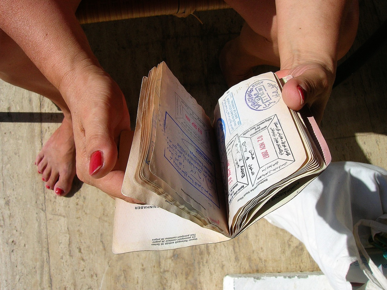 Kobieta siedząca na podłodze i przeglądająca paszport z pieczątkami w środku
