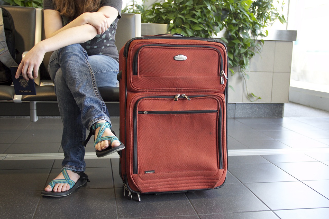 Kobieta z dużą czerwoną walizką podróżną, siedząca na krzesełku na lotnisku